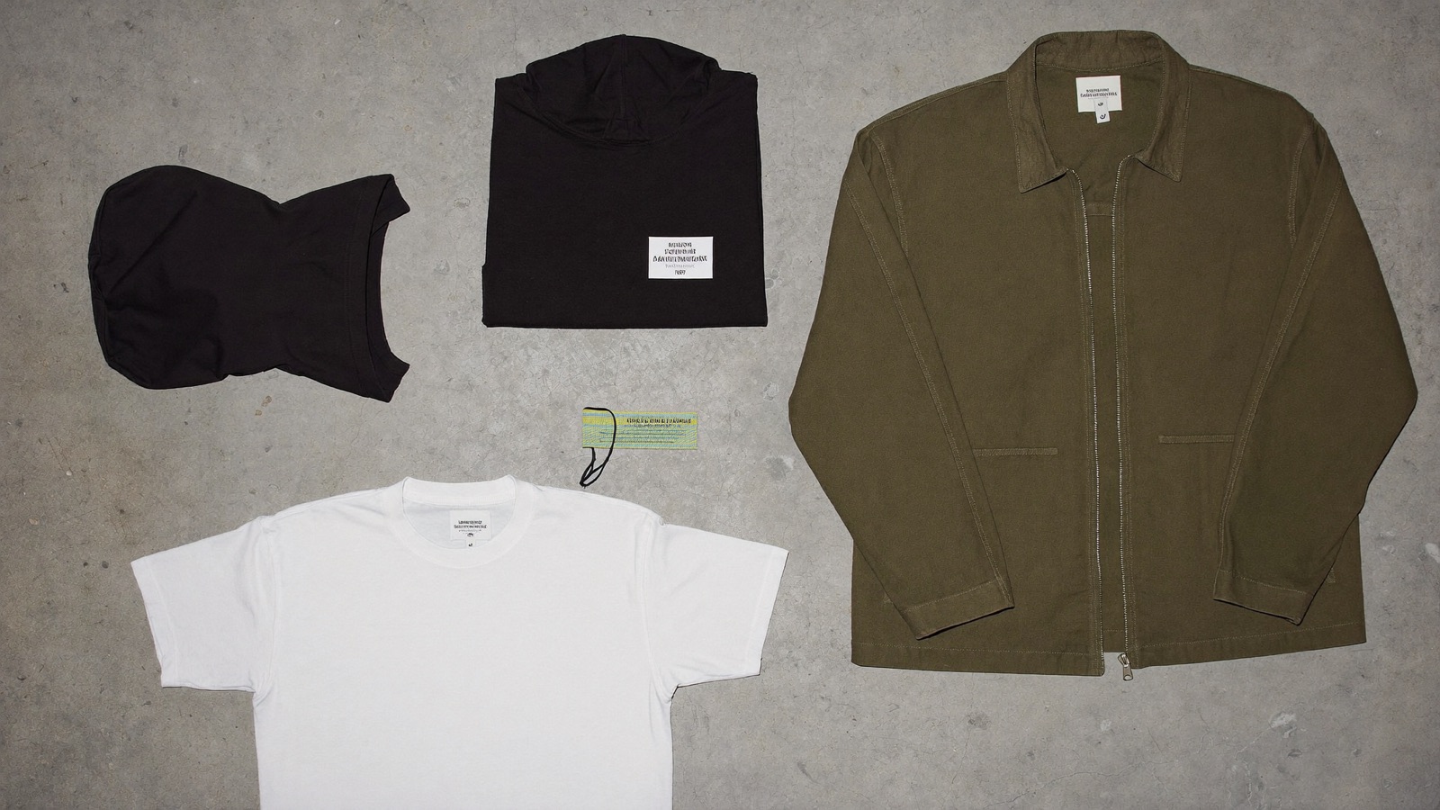Overhead flash photo of Drop 07 garments laid flat on raw concrete
